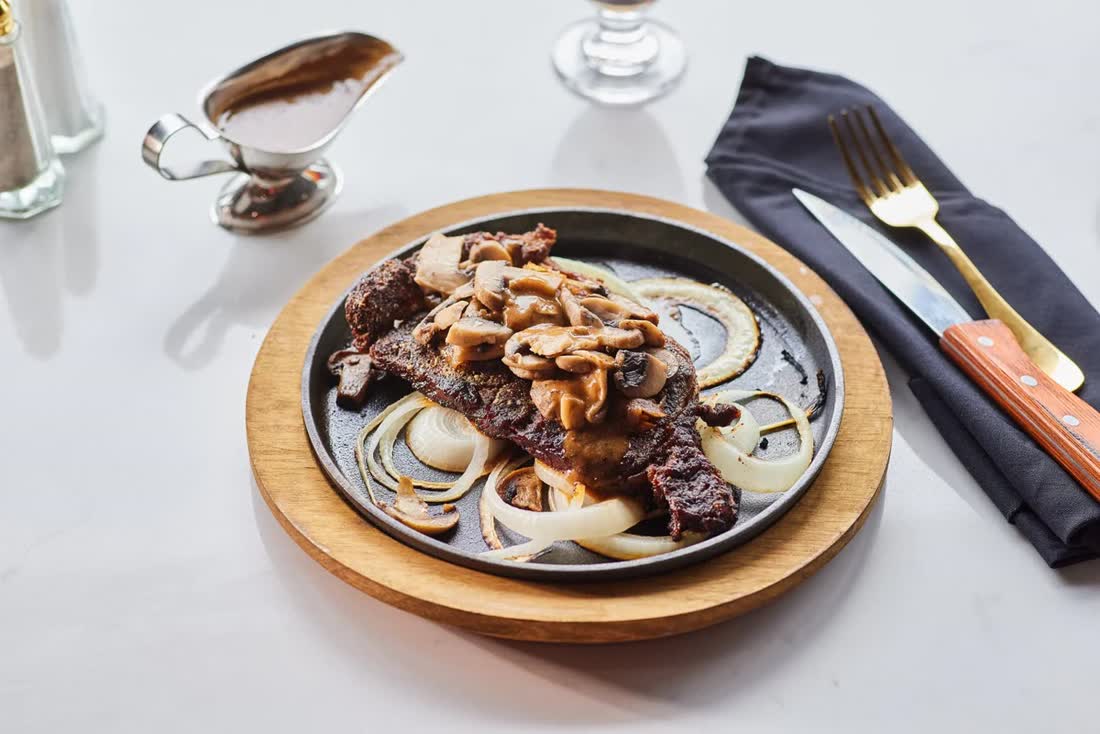 Halal New York strip steak with mushroom gravy on a cast iron skillet at Affy's Brooklyn